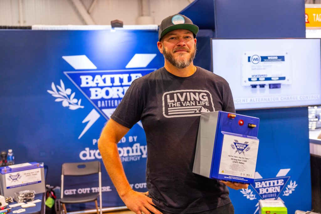 Filmmaker Chad DeRosa is wearing a baseball cap, a "Living the Van Life" Tshirt and holding a Battle Born Battery